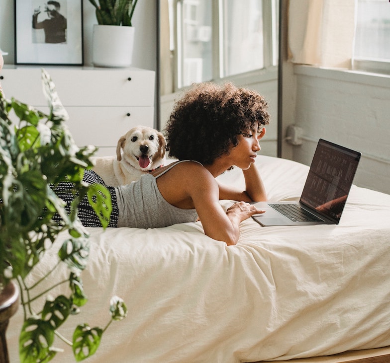 Pige og hund på seng med computer. De blogger